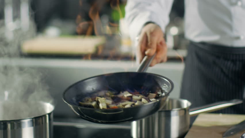 Professional Chef Cooks Flambe Style. He Prepares Dish in a Pan with Open Flames. He Works in a Modern Kitchen with Different Ingredients Lying Around.  Shot on RED EPIC-W 8K Helium Cinema Camera. Royalty-Free Stock Footage #28204183