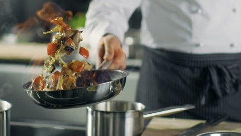Professional Chef Cooks Flambe Style. He Prepares Dish in a Pan with Open Flames. He Works in a Modern Kitchen with Different Ingredients Lying Around.  Shot on RED EPIC-W 8K Helium Cinema Camera.