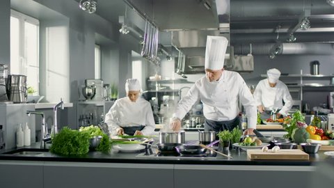 Famous Chef Works in a Big Restaurant Kitchen with His Help. Kitchen is Full of Food, Vegetables and Boiling Dishes. Shot on RED EPIC-W 8K Helium Cinema Camera.