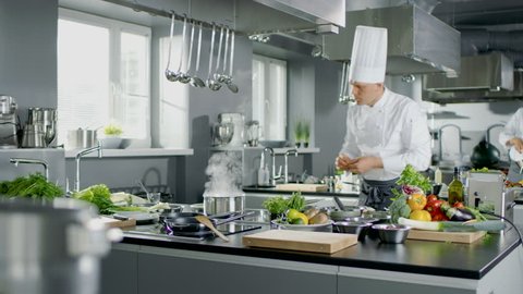 Famous Chef Works in a Big Restaurant Kitchen with His Apprentices. Kitchen is Full of Food, Vegetables and Boiling Dishes. Shot on RED EPIC-W 8K Helium Cinema Camera.