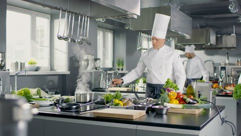 Famous Chef Works in a Big Restaurant Kitchen with His Apprentices. Kitchen is Full of Food, Vegetables and Pans on Fire. Shot on RED EPIC-W 8K Helium Cinema Camera.