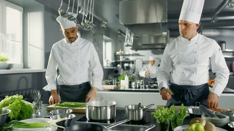 Two Famous Chefs Work as a Team in a Big Restaurant Kitchen. Vegetables and Ingredients are Everywhere, Kitchen Looks Modern with Lots of Stainless Steel.   Shot on RED EPIC-W 8K Helium Cinema Camera.