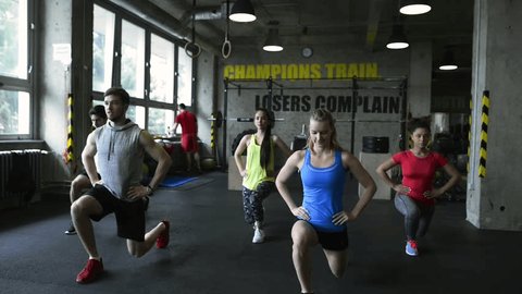 Young people in crossfit gym doing walking lunges.