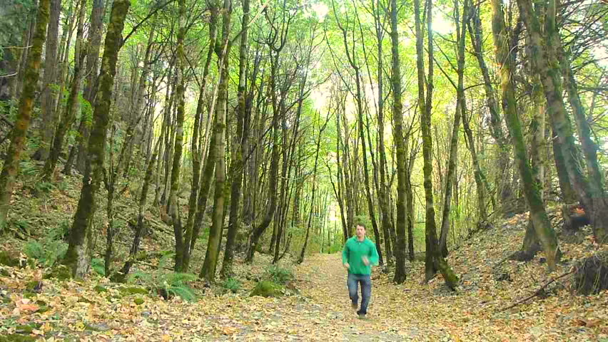 Man jogging in dense forest on trail full of leaves in Oregon.