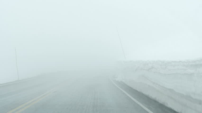 Driving Plate-POV-Trail Ridge Road snow lined with deep snow banks along road in Rocky Mountain National Park, Colorado with light snow falling on windshield with dense fog limiting visibility