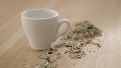 Ginger, Lemongrass, Hibiscus, Calendula Herbal Tea being poured into a tea cup on wood bench top, showing dried loose leaf tea leaves. High quality Pro Res 422 HQ footage.