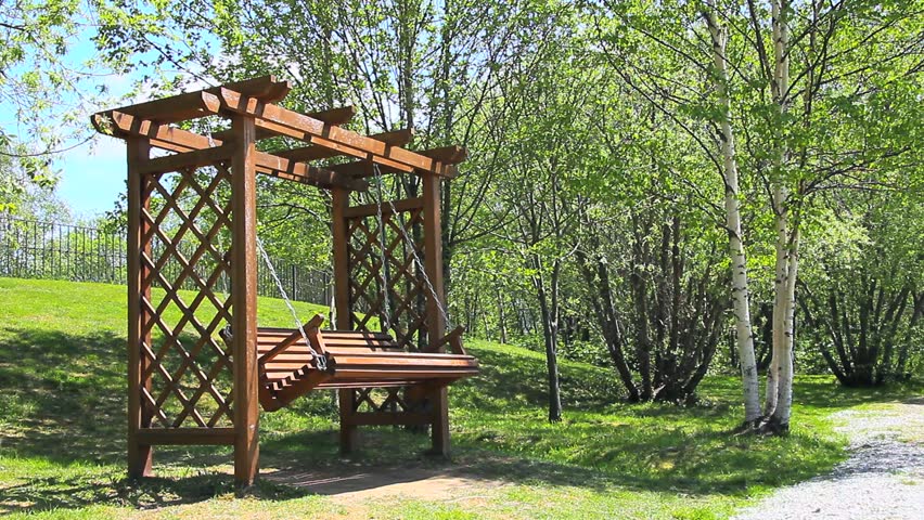 A video of a swing bench in a park, with people playing and laughing in the background