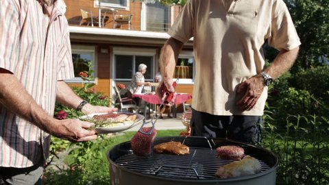 retirees putting beef on kettle barbecue in garden
