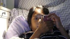 A very sleepy little Asian girl enjoys spending time in her home made fort in her bedroom listening to music and watching videos on her device while trying hard to not fall asleep. 
