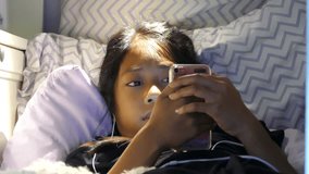 A very sleepy little Asian girl enjoys spending time in her home made fort in her bedroom listening to music and watching videos on her device while trying hard to not fall asleep. 