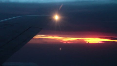 Airplane wing vibrates in strong winds as it flies over sunset. 