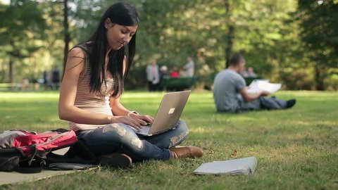 Young female student with modern laptop in the park
