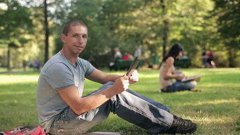 Young happy student with tablet computer in the park, steadicam shot
