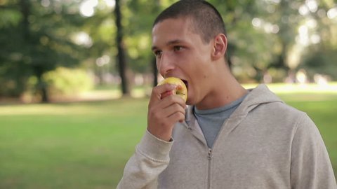 Young happy man eating apple in the park
