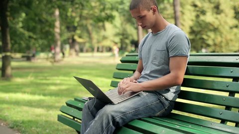 Young happy man with laptop relaxing in the city park, 