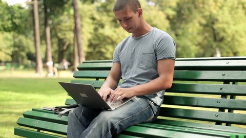 Young man with laptop sitting in the park
