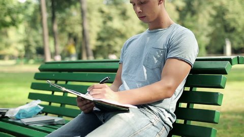Young student doing homework in the park
