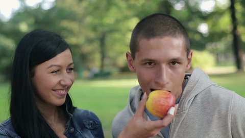 Happy couple eating apple in the park
