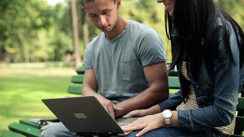 Young happy students with laptop in the park