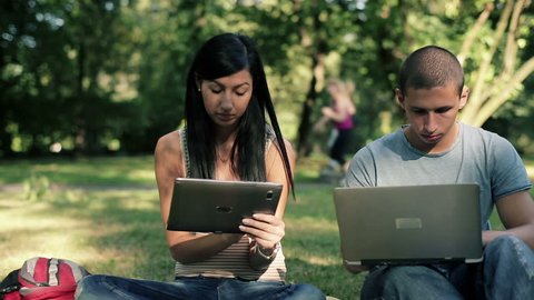 Happy students with laptop and tablet in the park