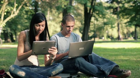 Young students with laptop and tablet in the park