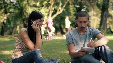 Young students with cellphone and notebook in the park