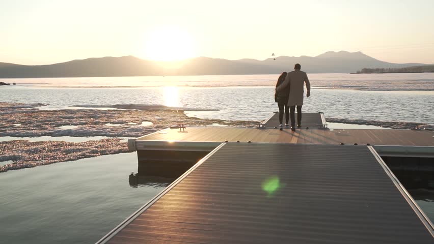 Frozen but happy couple in love walks on the pier at sunset