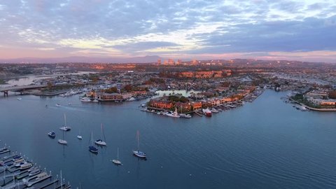 Aerial sunset shot with a drone over Newport Beach harbor with Linda Isle island, Pacific Coast Highway or PCH and Fashion Island in the background with pink skies.