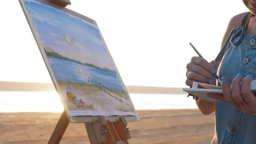 Young woman artist painting landscape in the open air on the beach, close up