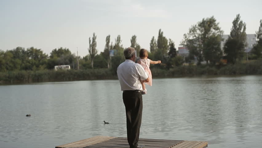 Grandfather with his granddaughter taking a walk by the lake
