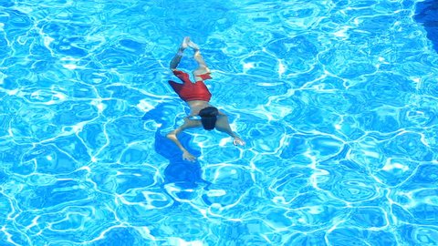 The child is swimming in the blue water of the pool. view from above. The boy dives under the water in the pool