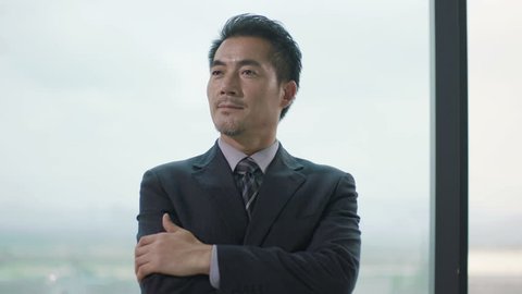 pensive asian corporate executive standing thinking by the window, arms crossed 