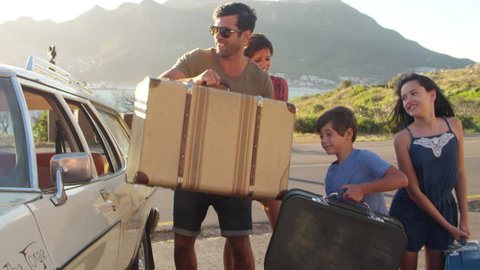 Family Loading Luggage Onto Car Roof Rack Ready For Road Trip