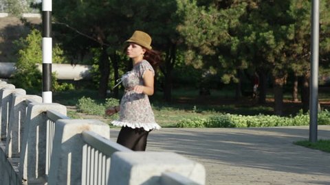 A girl dances in a hat. Goes for a walk on an embankment, dances and touches a fence