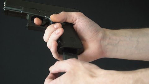 young man inserts the clip into gun black. slow motion.