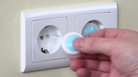 Hands install safety plugs in electricity outlet on wall (baby and child safety concept)