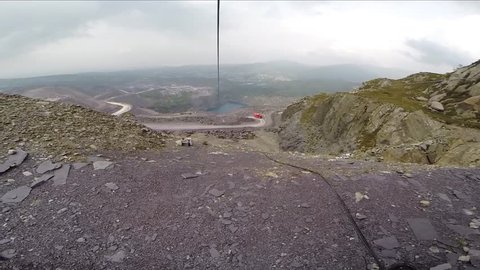 A Point of view footage clip of an exciting, extreme zipline experience, high above vivid green trees and a blue water slate quarry on a gloomy day in wales. flying experience.