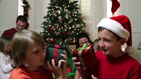 Two young boys in a family Christmas scene shake their presents as if trying to determine the contents.