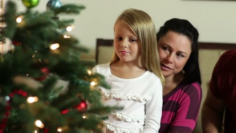 The camera pans down from a cute little girl and her mom to another sitting on the floor next to the Christmas tree