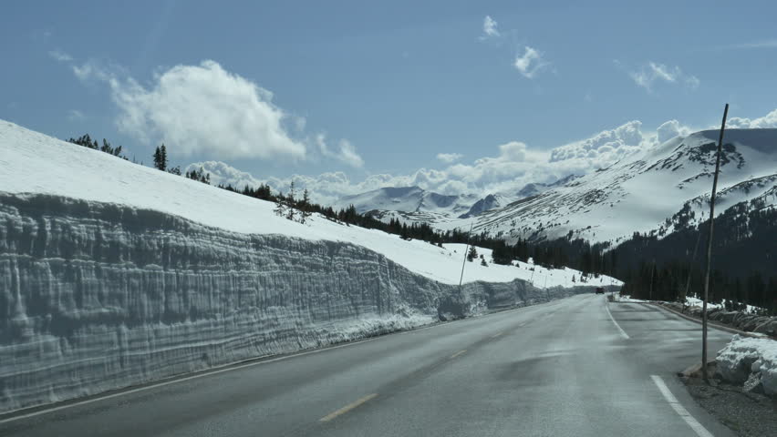 Drive Plate-Deep snow and pine trees line the highway along Trail Ridge Road in Rocky Mountain National Park, Colorado with beautiful snow capped mountains, blue sky and fluffy white clouds.