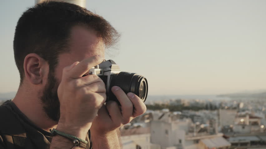 A young passionate photographer using a vintage film camera to photograph the city during sunset from a high angle | Shutterstock HD Video #28293601