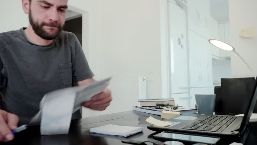 Young man overwhelmed by his bills at home.A young man at home calculates his living expenses and sums his bills and his overdue notices and falls into despair Royalty-Free Stock Footage #28294954