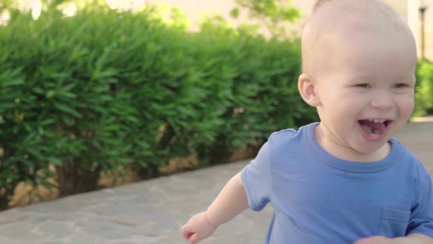 Portrait of a cute smiling blond boy enjoying a walk in a beautiful summer park, slow motion. Child walks along the alley with beautifully clipped green bushes, a well-groomed modern summer park | Shutterstock HD Video #28297336