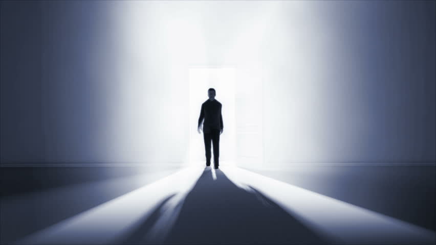 A man walking in a dark room with a strong light coming from behind