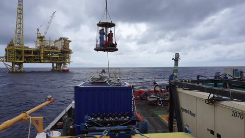 SARAWAK, MALAYSIA - JUNE 12th, 2017: Unidentified workers using personal transfer basket during crews change with background of offshore drilling platform at South China Sea, Malaysia.
