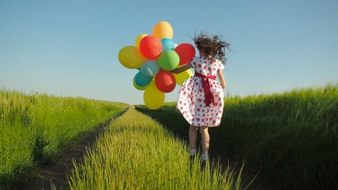Little girl in a field with balloons. Happy child runs in a wheat field with balloons.