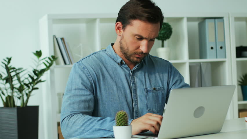 Serious young business man in blue shirt working on the laptop in the office, he feeling annoying headache.
