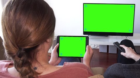 Girl Watch Tablet And Man Watch TV Green Screen, Pan Camera. Pan camera on couple watching television and tablet green screen. Shot behind models shoulders