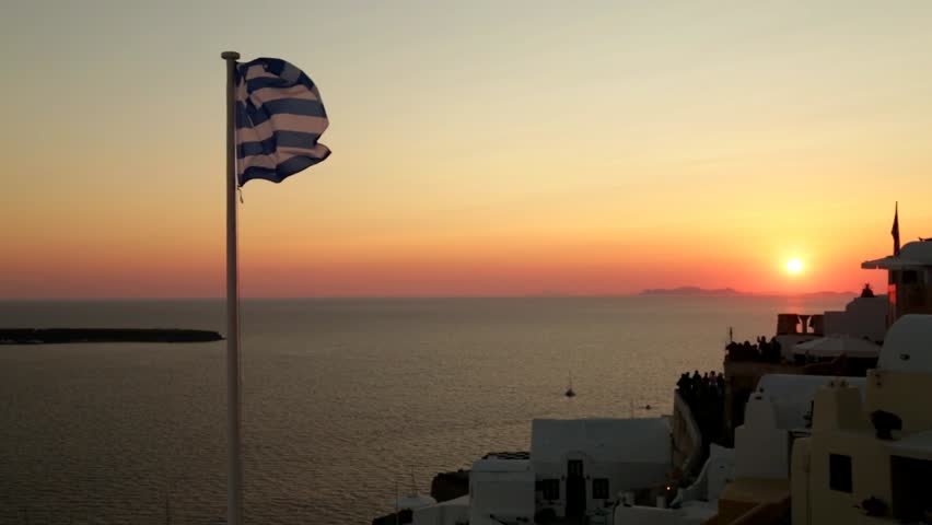 Greek flag waving at sunset in Oia, Santorini, Greece