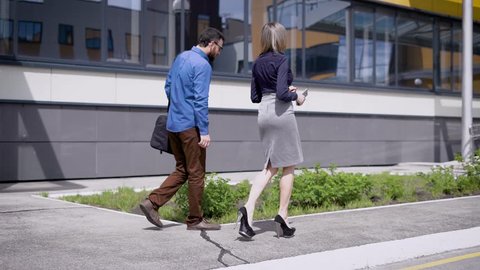 Business people at office building. Back view of business man and woman walking and communicating near urban office building.